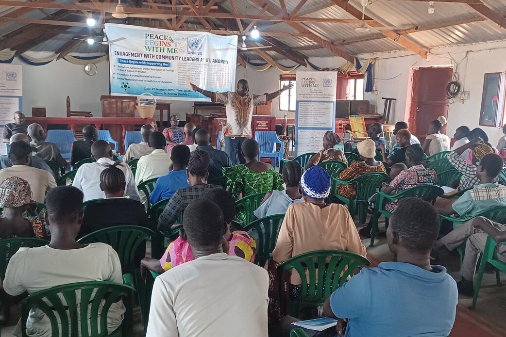 Freedom of expression and inclusion in preparations for elections were the hot topics at an UNMISS-hosted dialogue for 80 members of the Gudele community in Juba. A group of people seated in green plastic chairs seated facing a stage where a man is presenting with their arms outstretched.