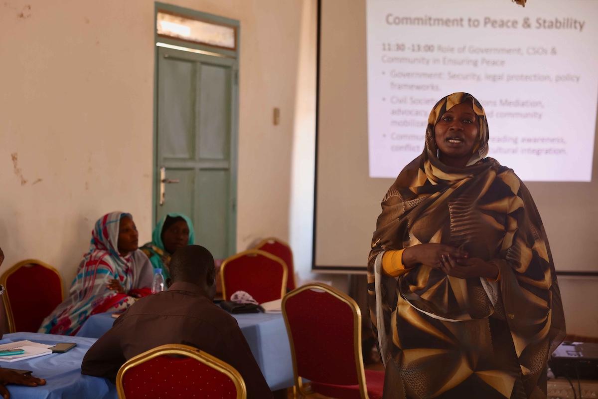 In January, intercommunal tensions in Kuajok boiled over due to events in neighbouring Sudan. Representatives from the different communities have now met in a bid to reconcile. Photos: Zejin Yin/UNMISS A woman addressing a group of people seated at tables. In the background, there is a PowerPoint presentation. that the woman is presenting.
